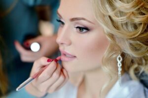 A close-up of a bride applying Luscious Lip Gloss, highlighting her radiant smile and perfect makeup for her special day.